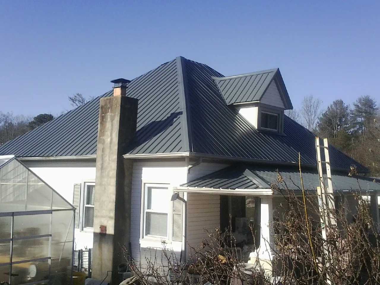 Dark blue standing seam metal roof on a white farmhouse with dormer — Slate & Tile Roof Repair by Roofing Brothers in Muir
