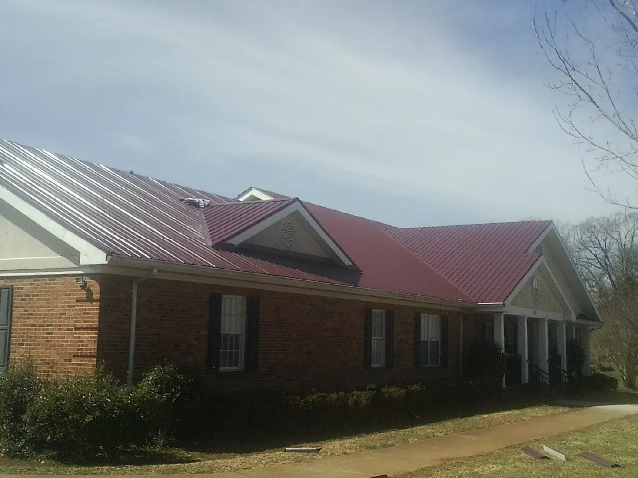 Red metal roof with gabled entries on a long brick building, from a Hail Damage Roof Repair job in Muir
