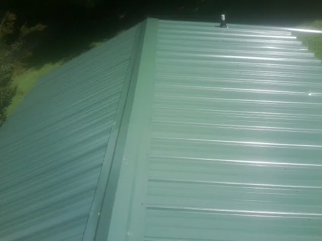 New green metal panels meeting at the ridge of a roof — Flat Roof Repair work by our crew in Muir