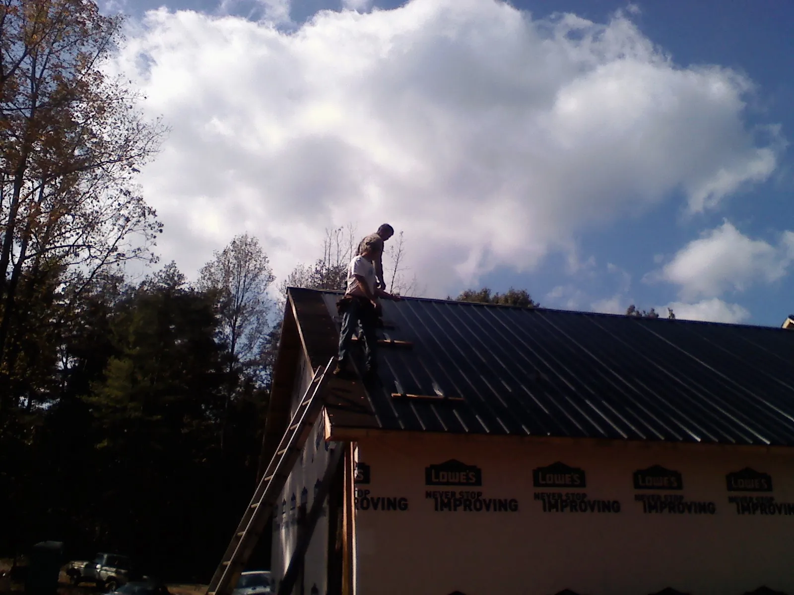 Roofer fastening dark metal panels high against a cloudy sky, from a Roof Inspection job in Muir