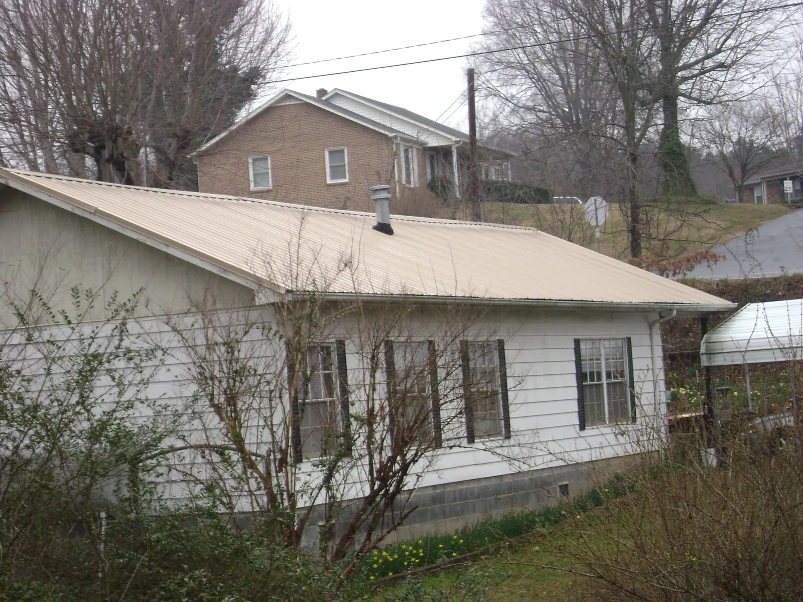 Tan metal roof on a white sided house set into a hillside — Commercial Roofing by Roofing Brothers in Muir